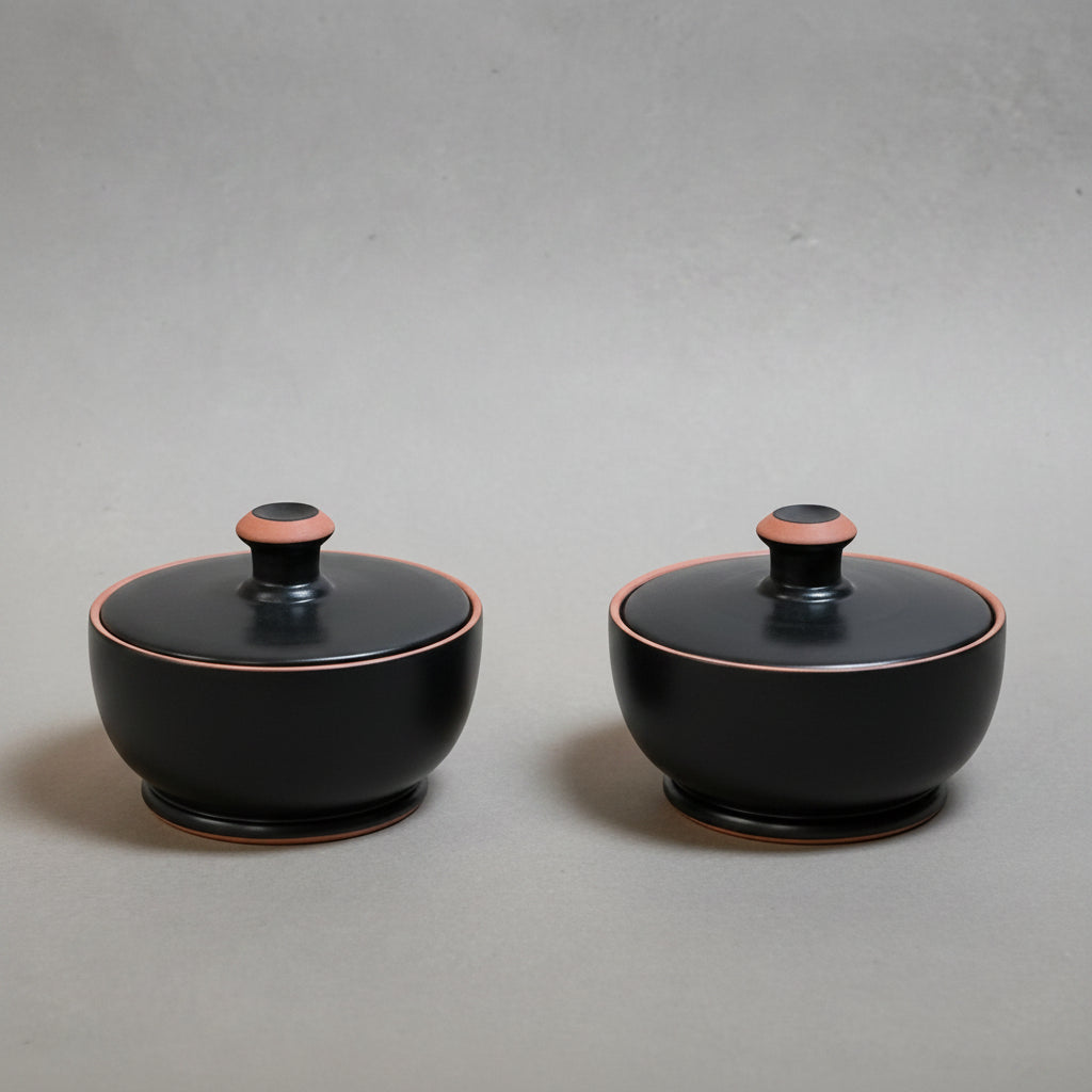 Two black ceramic containers - pyxis - with pink accents on a grey background