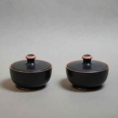 Two black ceramic containers - pyxis - with pink accents on a grey background