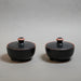 Two black ceramic containers - pyxis - with pink accents on a grey background