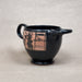 Black ceramic cup with pink and black design on a beige background