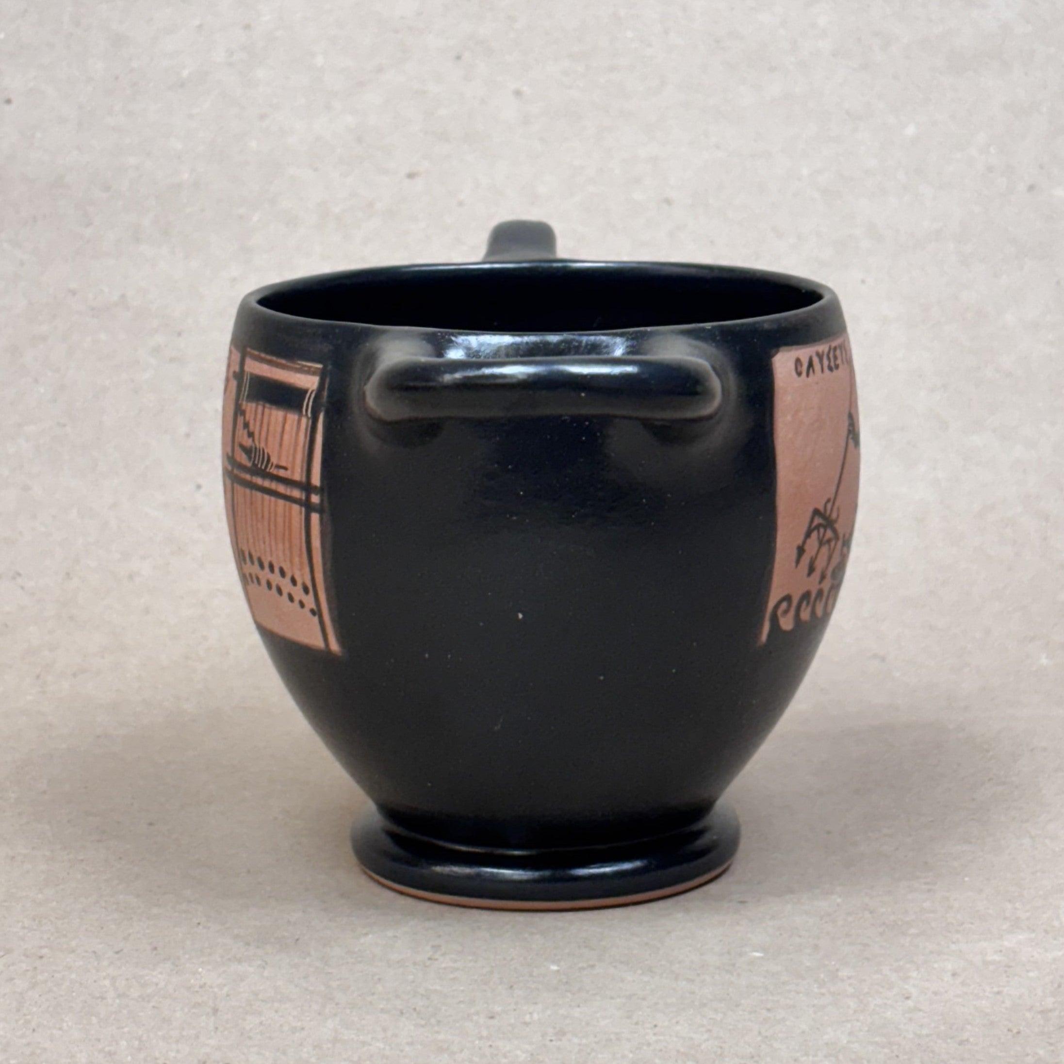 Black ceramic mug with pink geometric patterns on a beige background