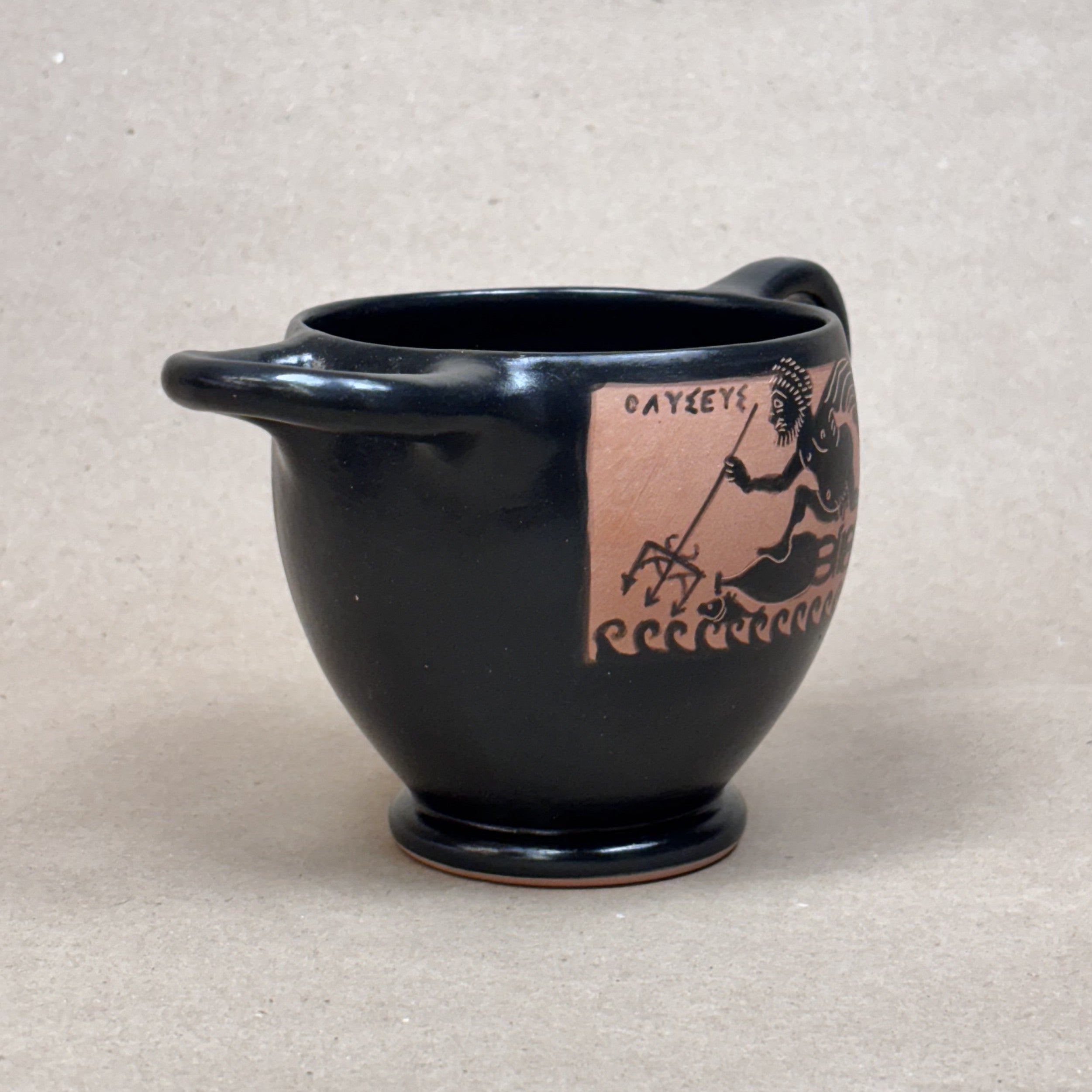 Black ceramic cup with a decorative handle and red graphic on a beige background