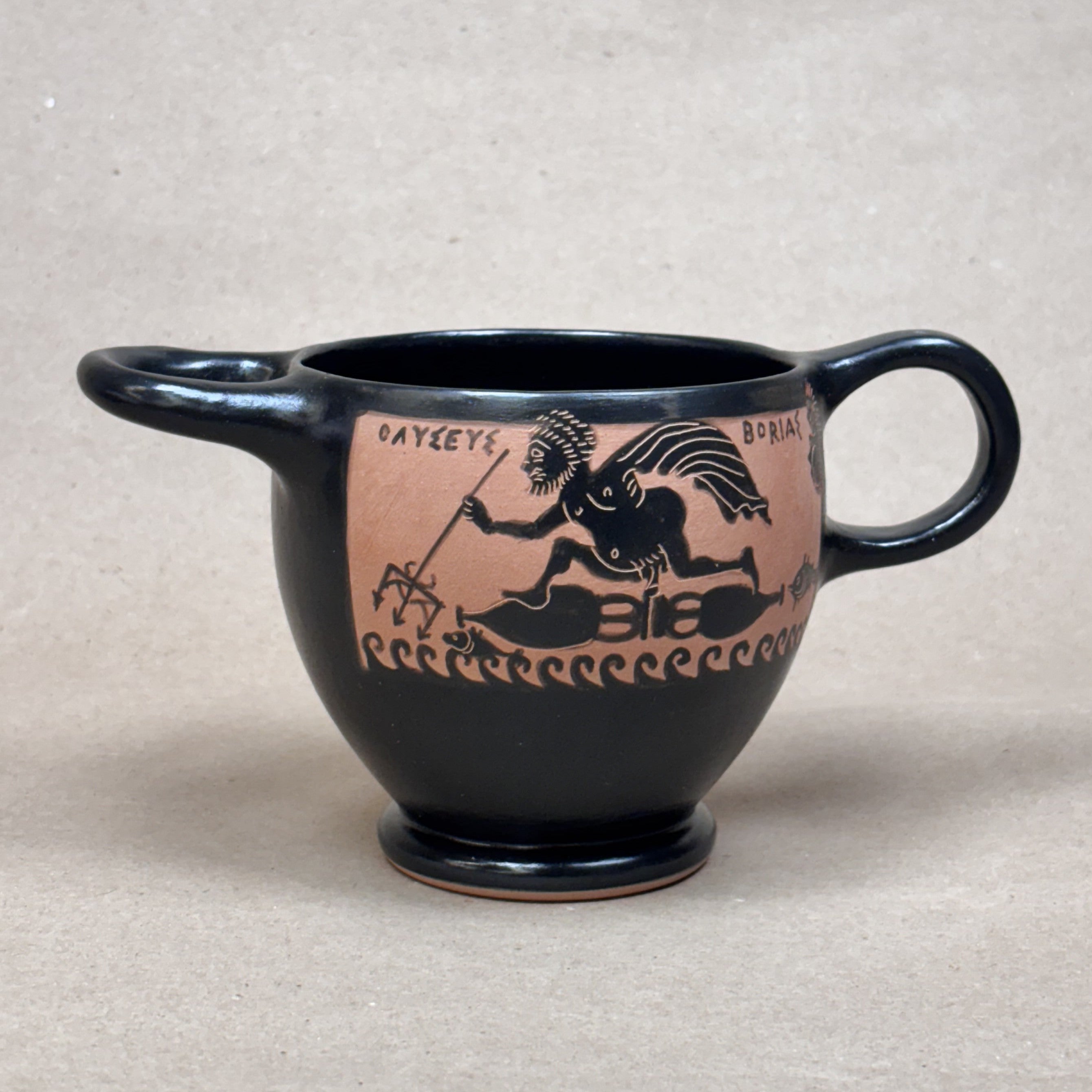 Black ceramic cup with ancient Greek design on a beige background
