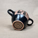 Black ceramic cup with pink and black designs on a beige background