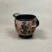 Ceramic cup with black handle and decorative design on a beige background