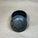 Black decorative container with lid on a beige fabric background