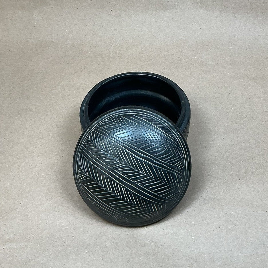Black decorative container with lid on a beige fabric background