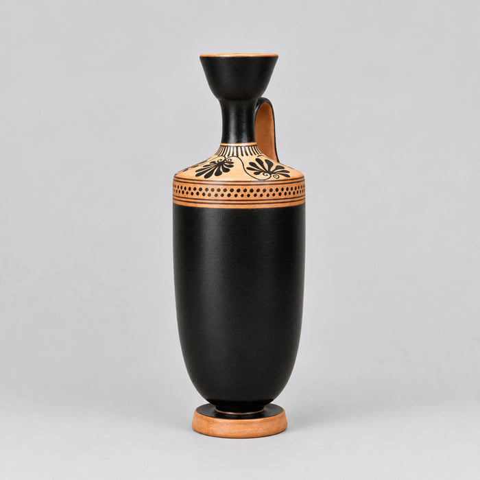 A black ceramic vase with a flared neck, a side handle, and a terracotta-colored base decorated with black geometric and floral patterns, set against a neutral beige background.