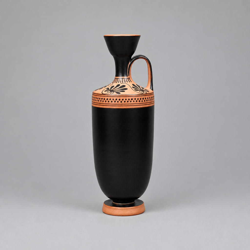 A black ceramic vase with a conical stopper, a side handle, and terracotta-colored decorative bands near the neck and base, photographed against a neutral textured beige backdrop.