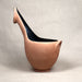 A sculptural ceramic pitcher with a curved neck and spout, made of terracotta-colored clay with a glossy black interior, set against a neutral light gray background.