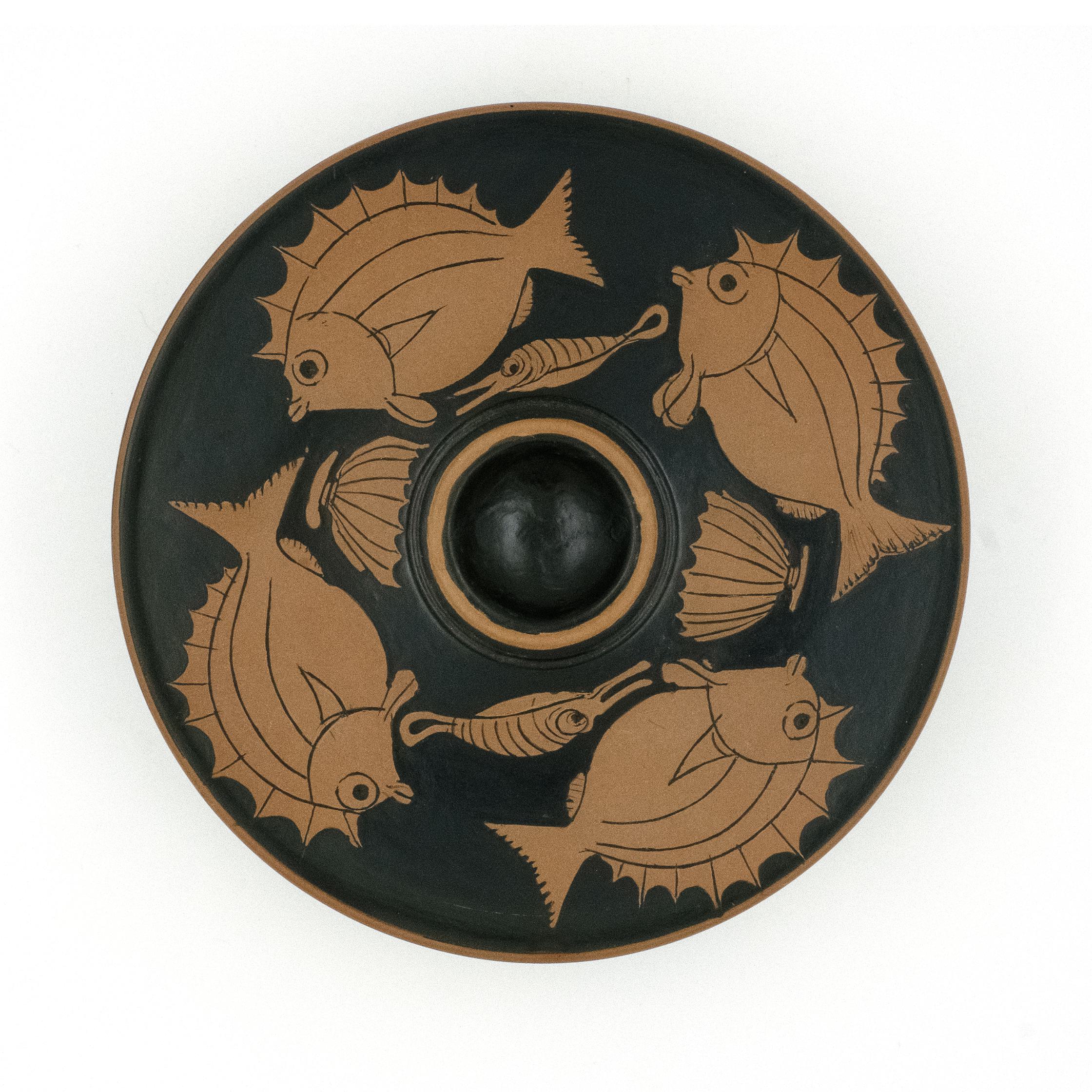 A round, black and red-figured ceramic plate with a central fish design and additional fish patterns around the border.