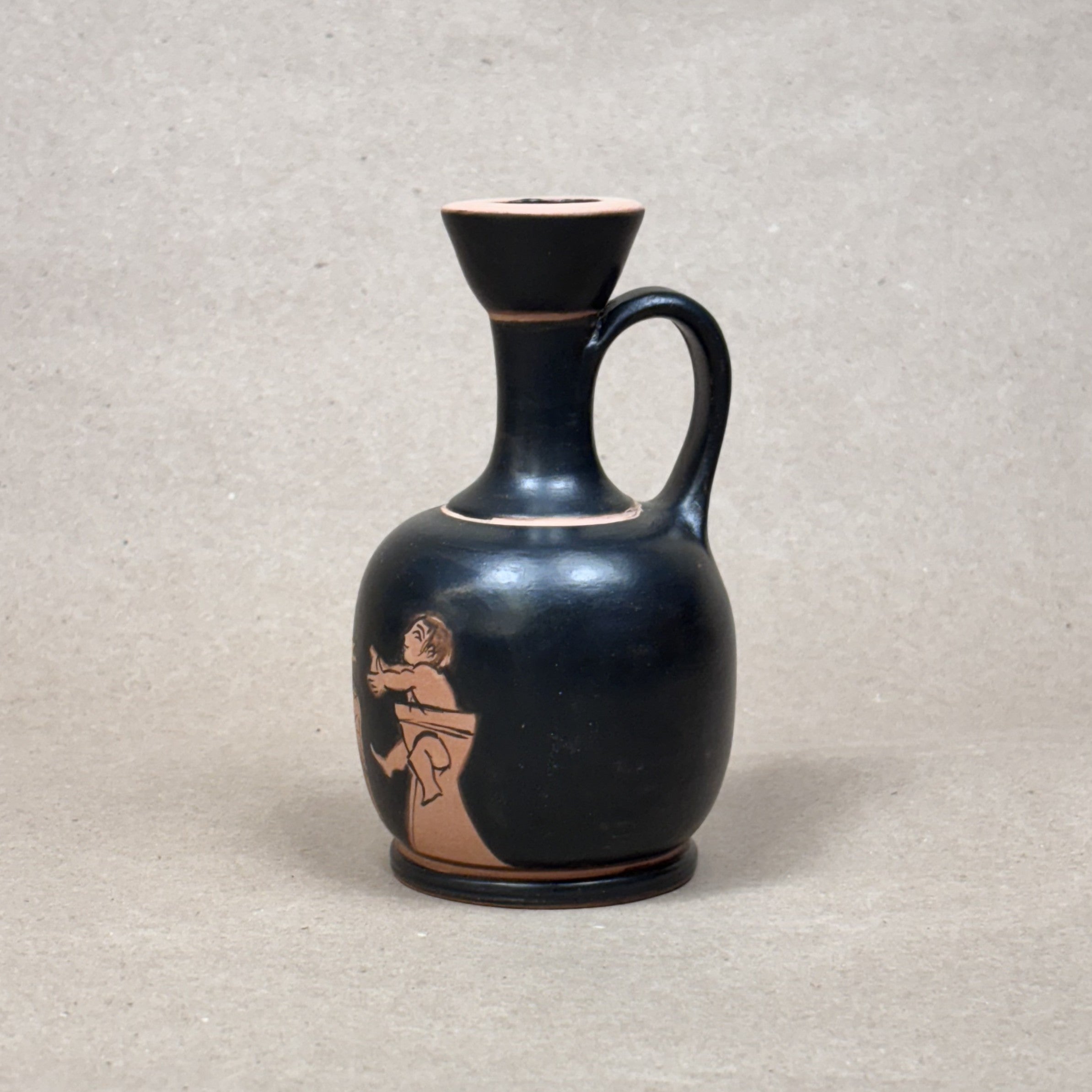 Black ceramic vase with a handle and red decorative design on a gray background