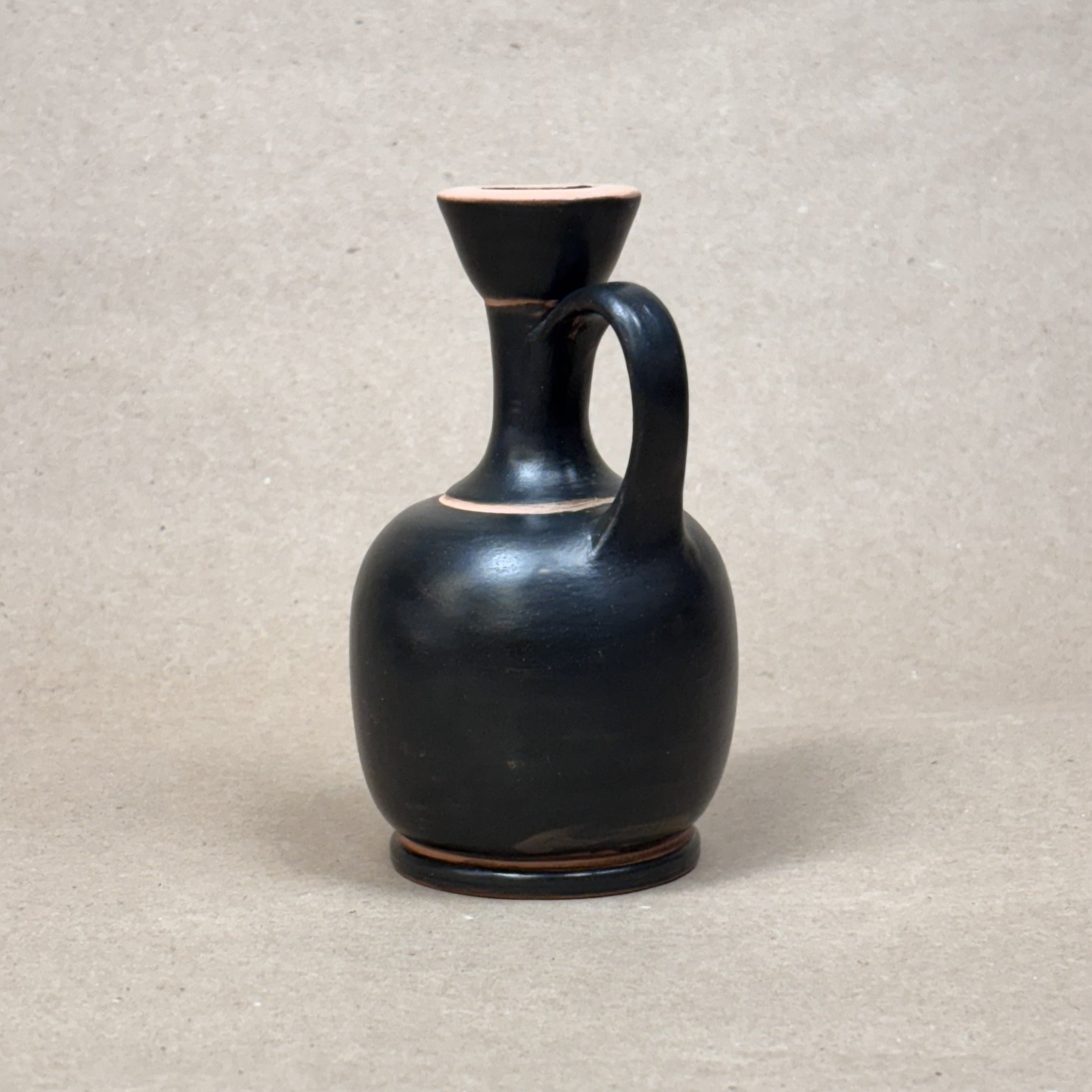 Black ceramic pitcher on a beige background