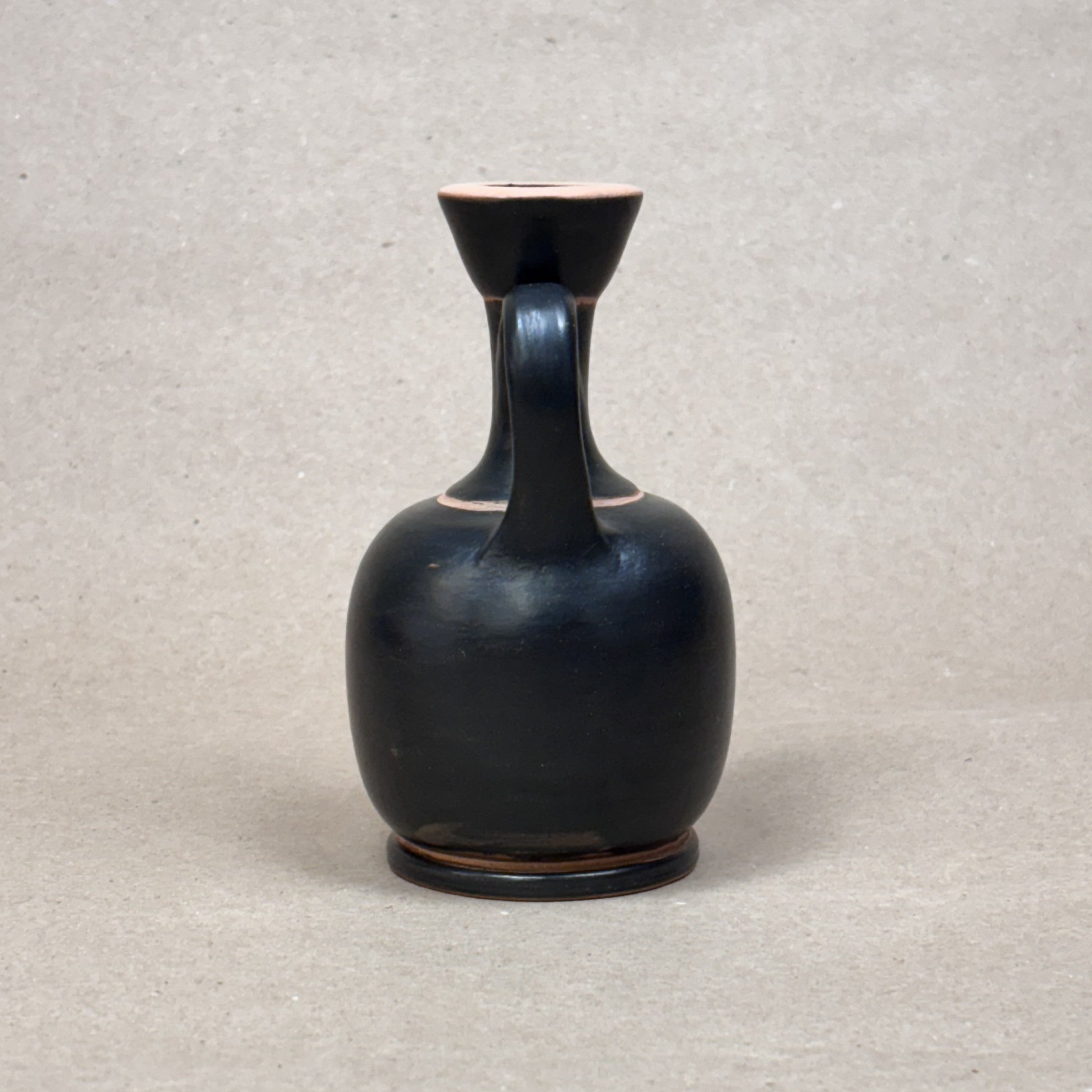 Black ceramic vase with a handle on a light gray background