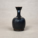 Black ceramic vase with a handle on a light gray background