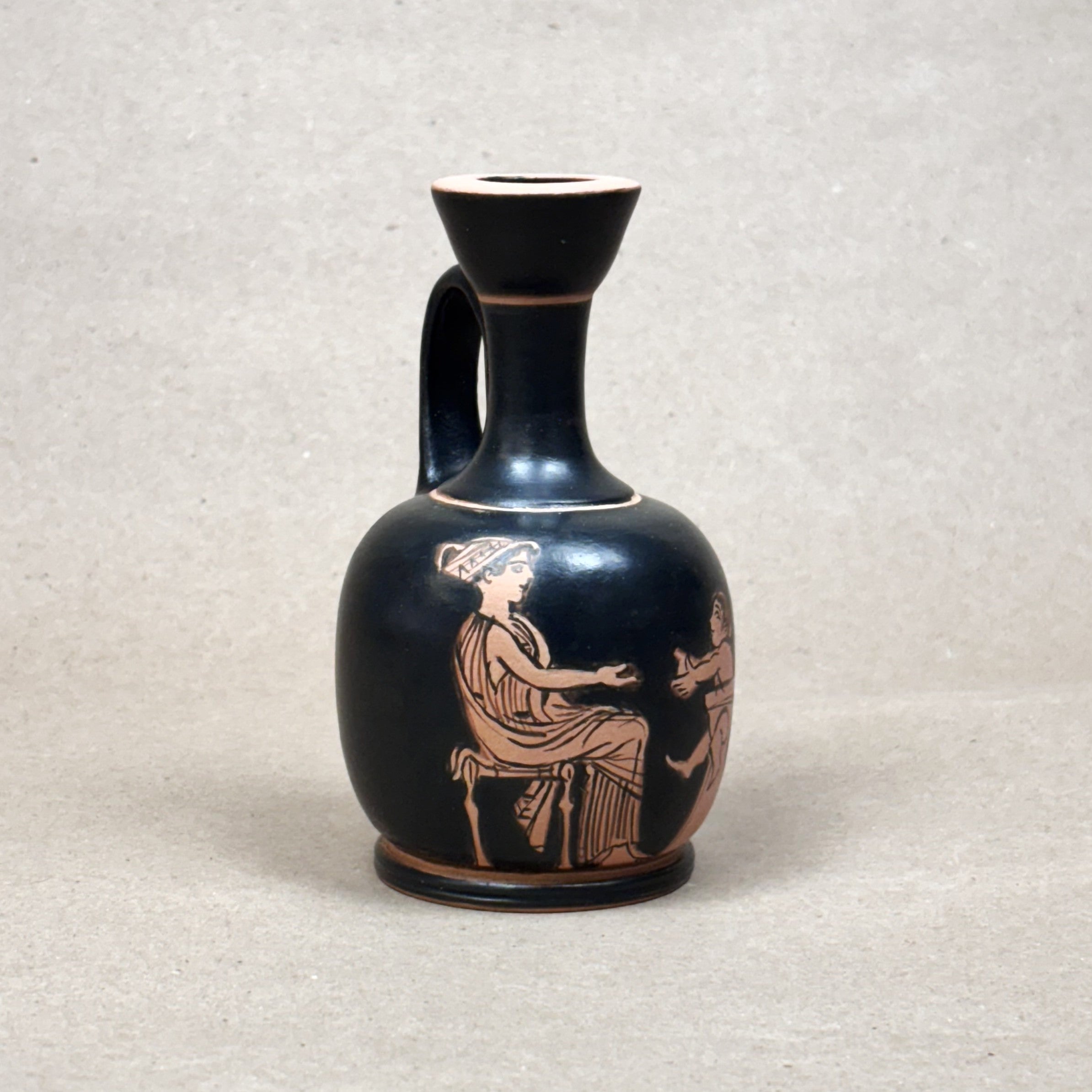 Black ceramic vase with red-figure decoration of a seated figure on a gray background