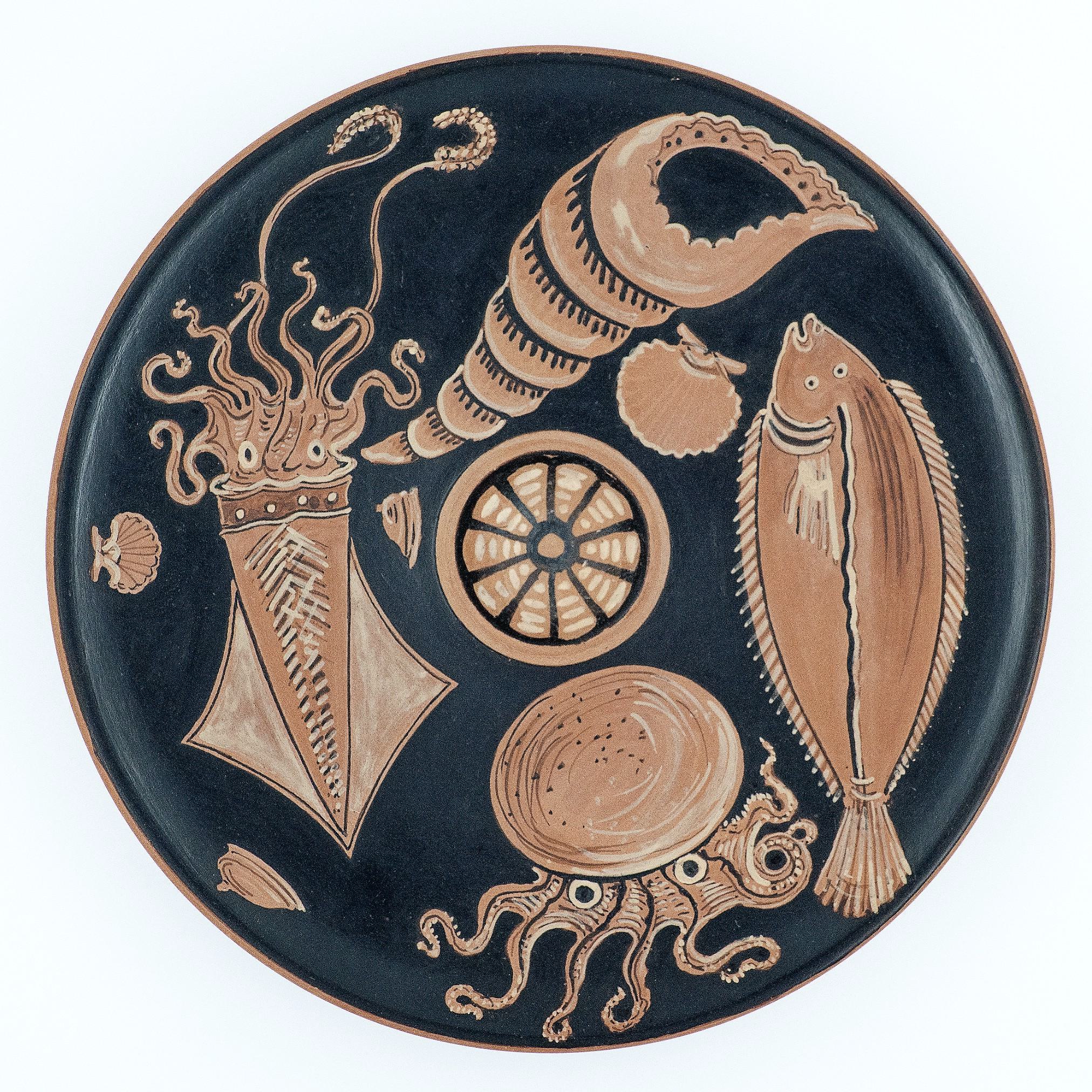 A photograph of a round ceramic plate with a reproduction of an Apulian Fish Plate design, featuring marine life including an octopus and various fish, primarily in brown tones on a black background.