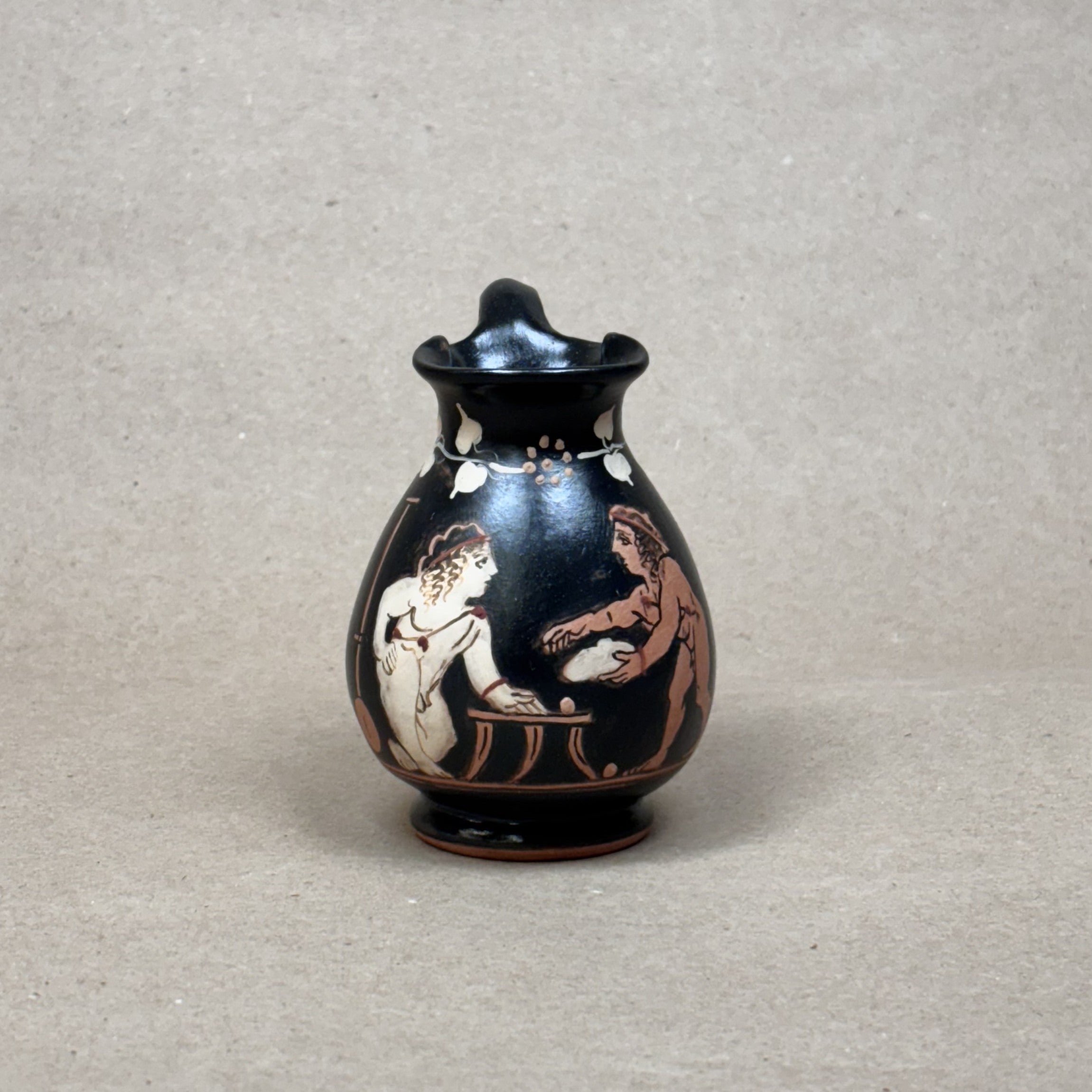 Small black vase with red and white figures on a gray background
