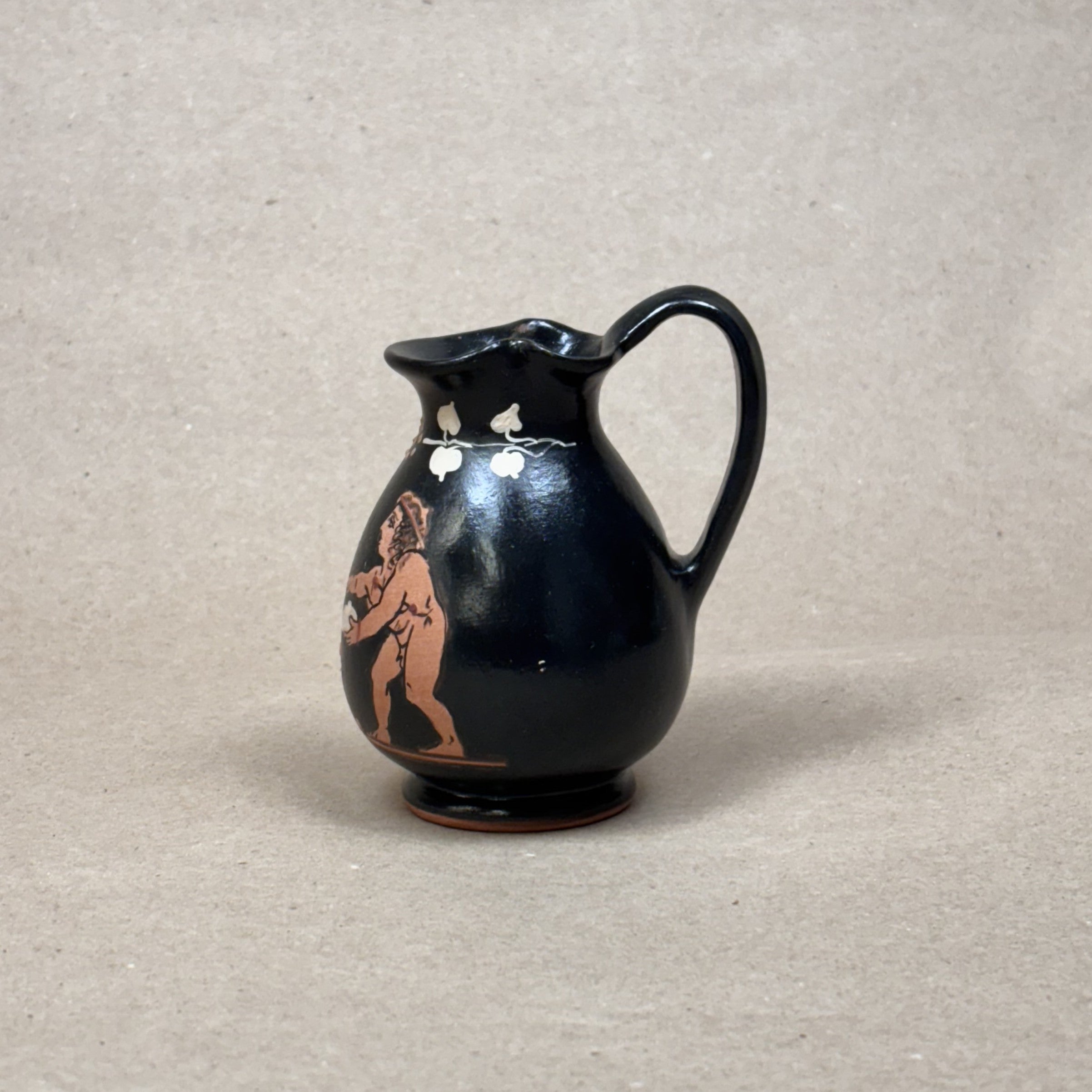 Black ceramic pitcher with red figurine on a beige background