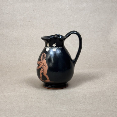 Black ceramic pitcher with red figurine on a beige background