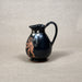 Black ceramic pitcher with red figurine on a beige background