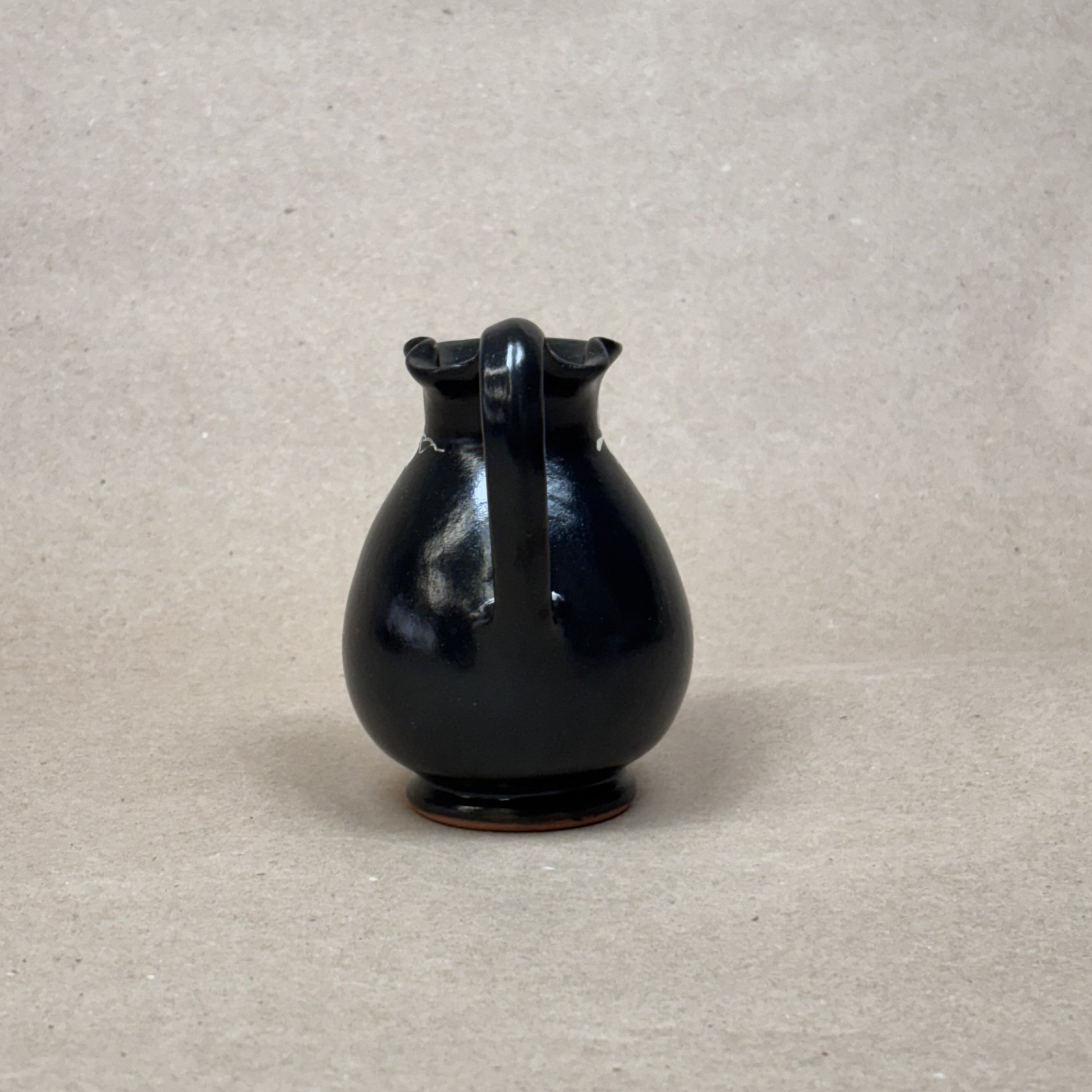 Black ceramic pitcher on a beige background