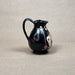 Black ceramic pitcher with white floral design on a beige background