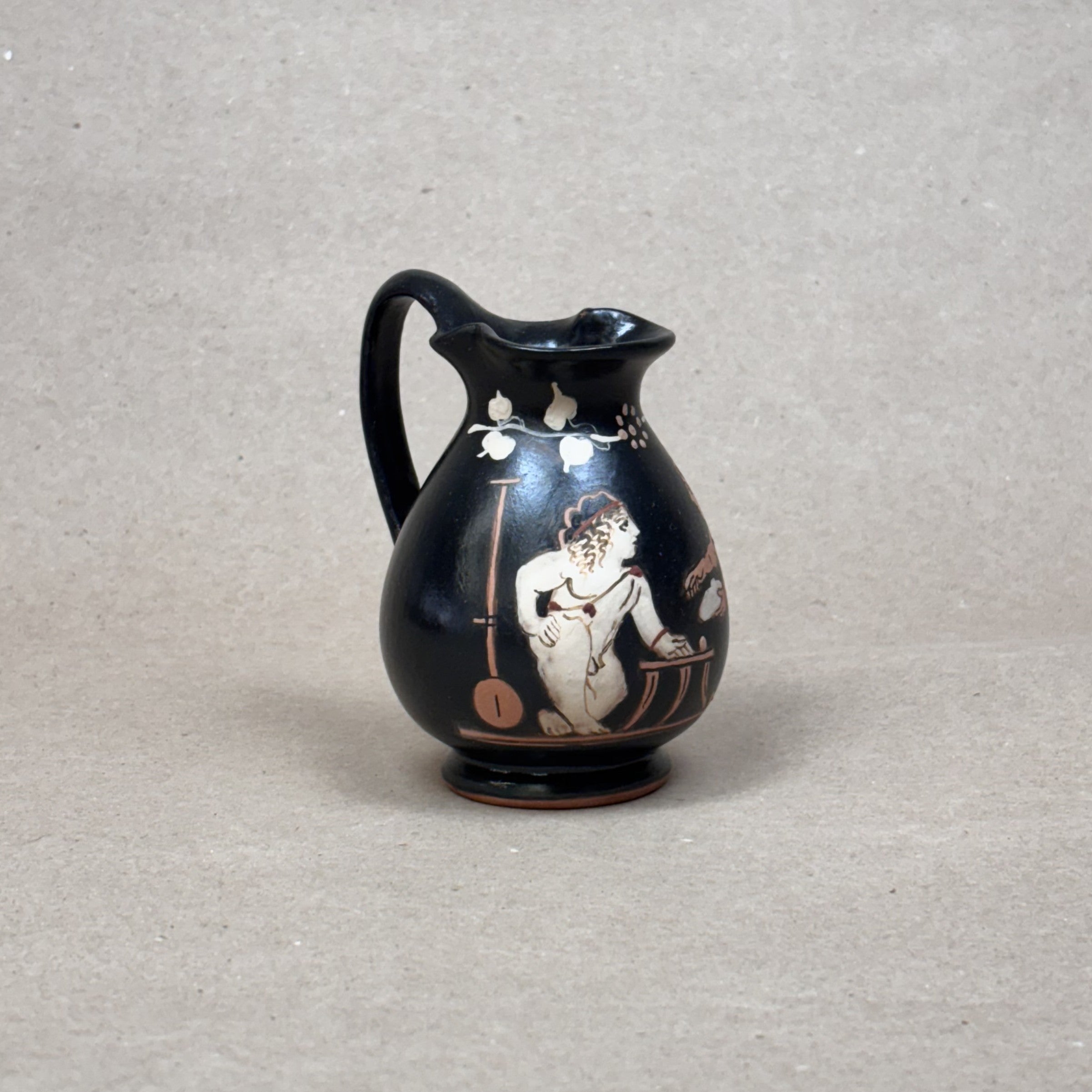 Black ceramic pitcher with white decorative design on a gray background