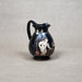 Black ceramic pitcher with white decorative design on a gray background