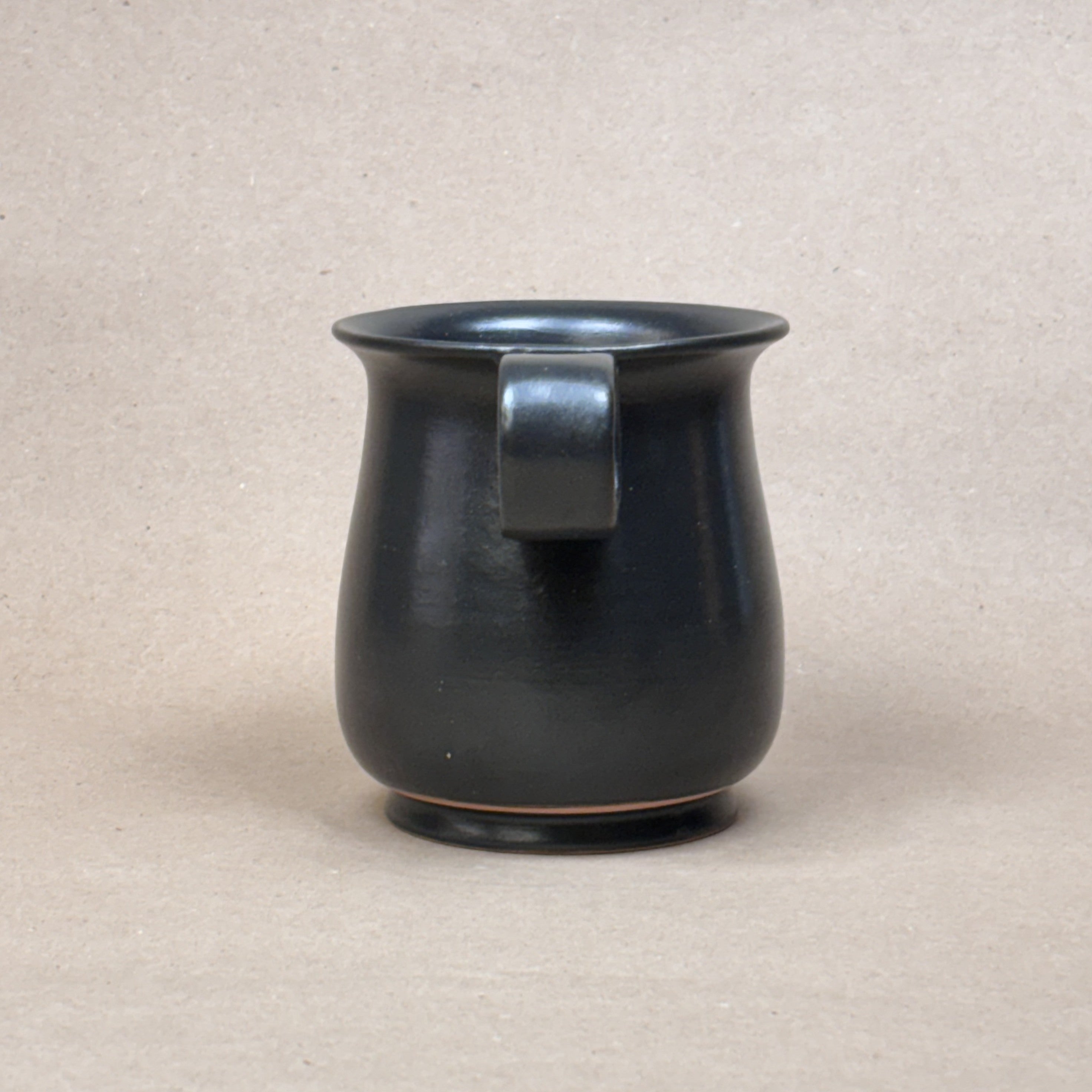 Black ceramic mug with handle on a beige background