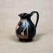 Black ceramic pitcher with decorative copper patterns on a beige background