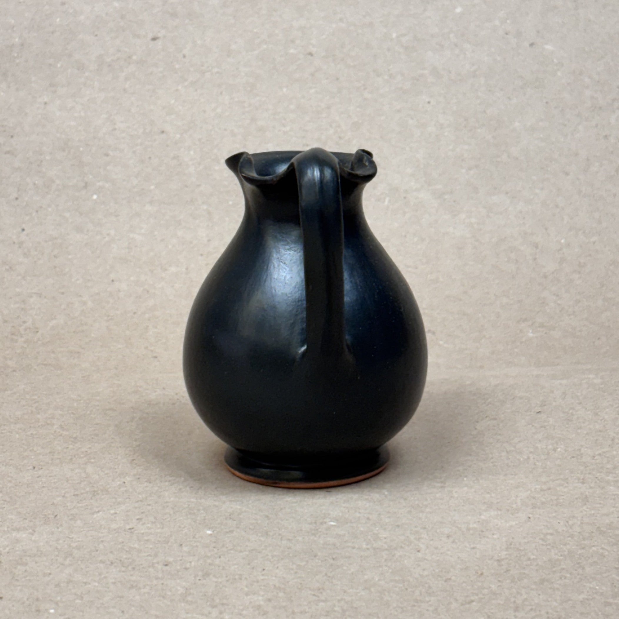 Black ceramic pitcher on a beige background