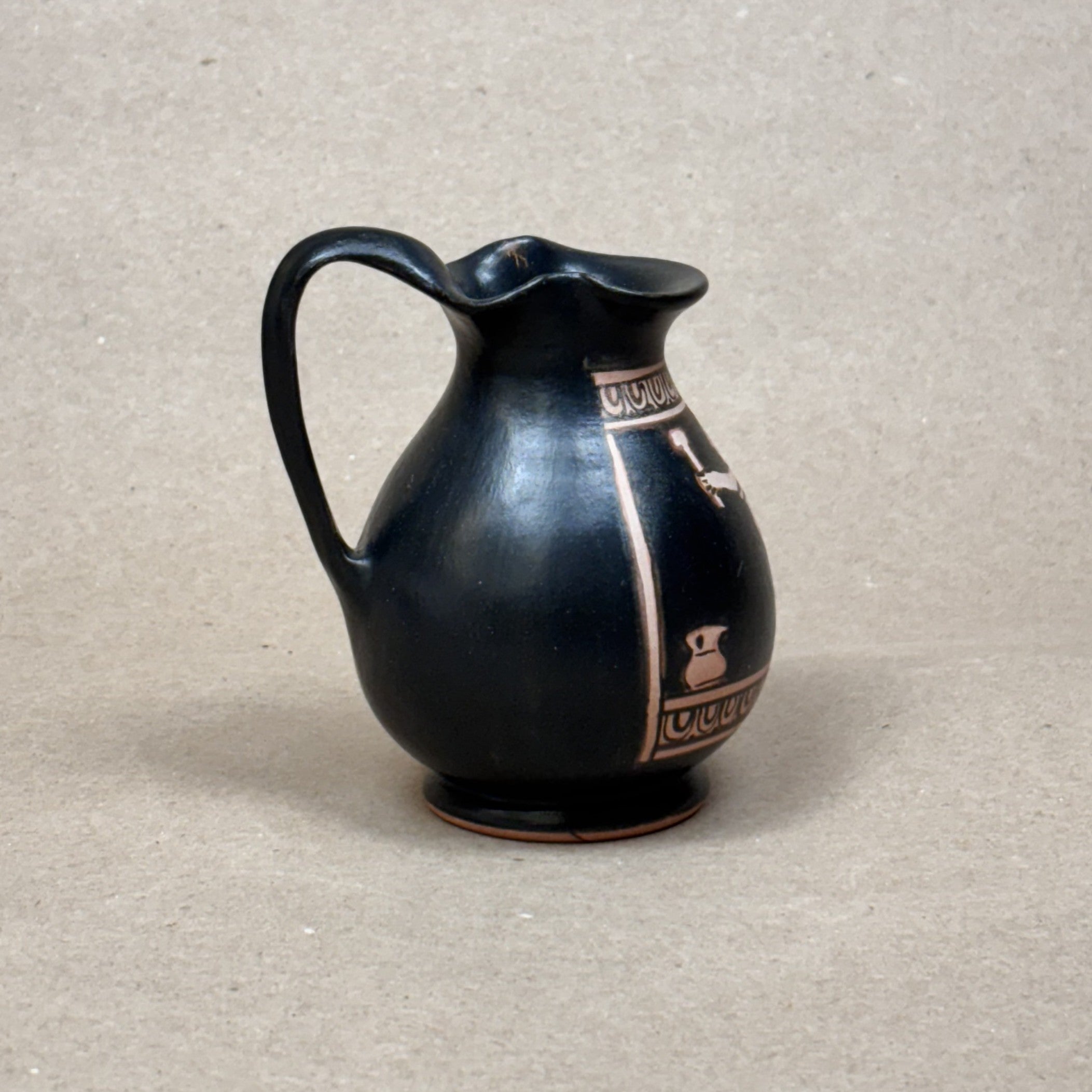 Black ceramic pitcher with decorative elements on a beige background