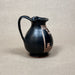Black ceramic pitcher with decorative elements on a beige background