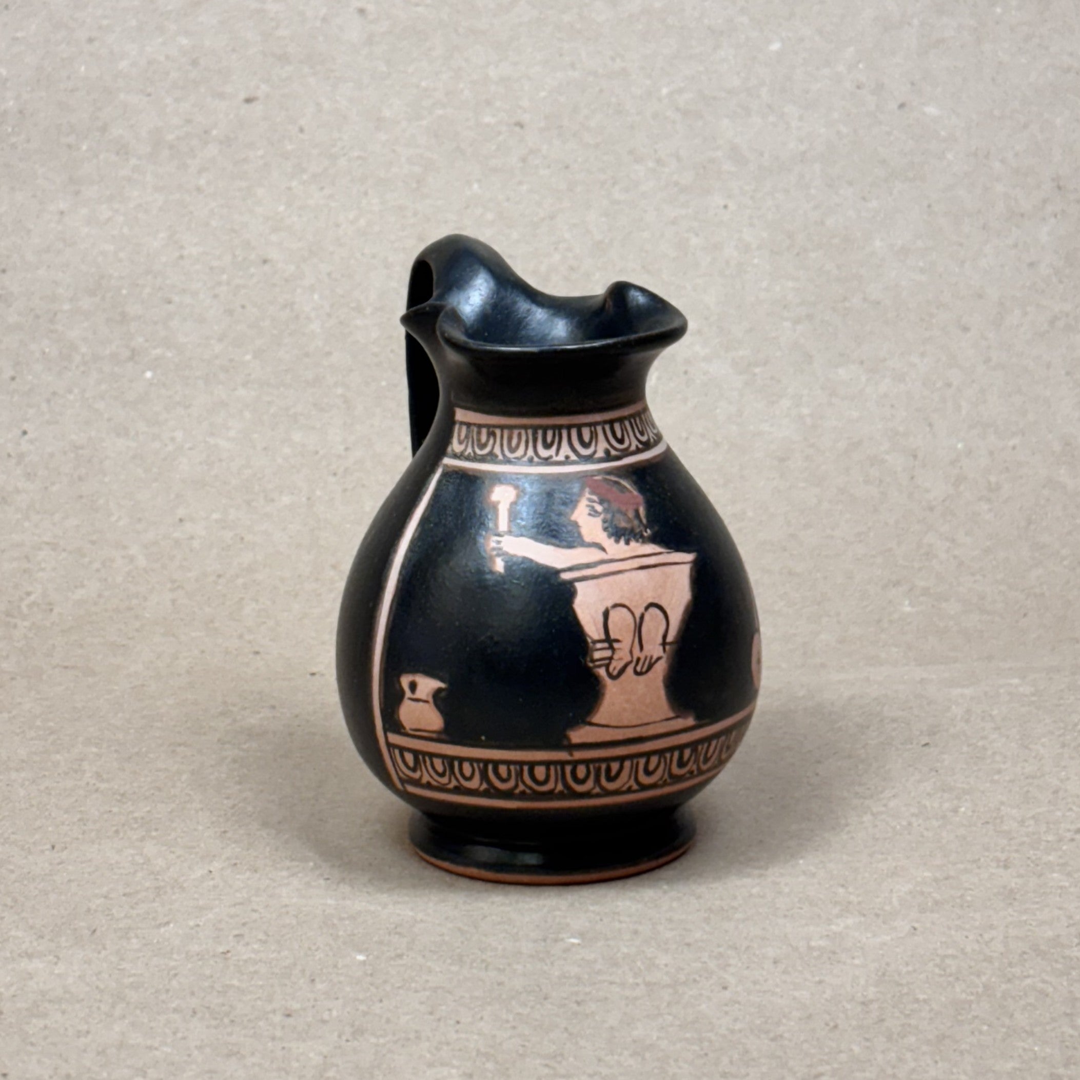 Black ceramic pitcher with red decorative patterns on a gray background