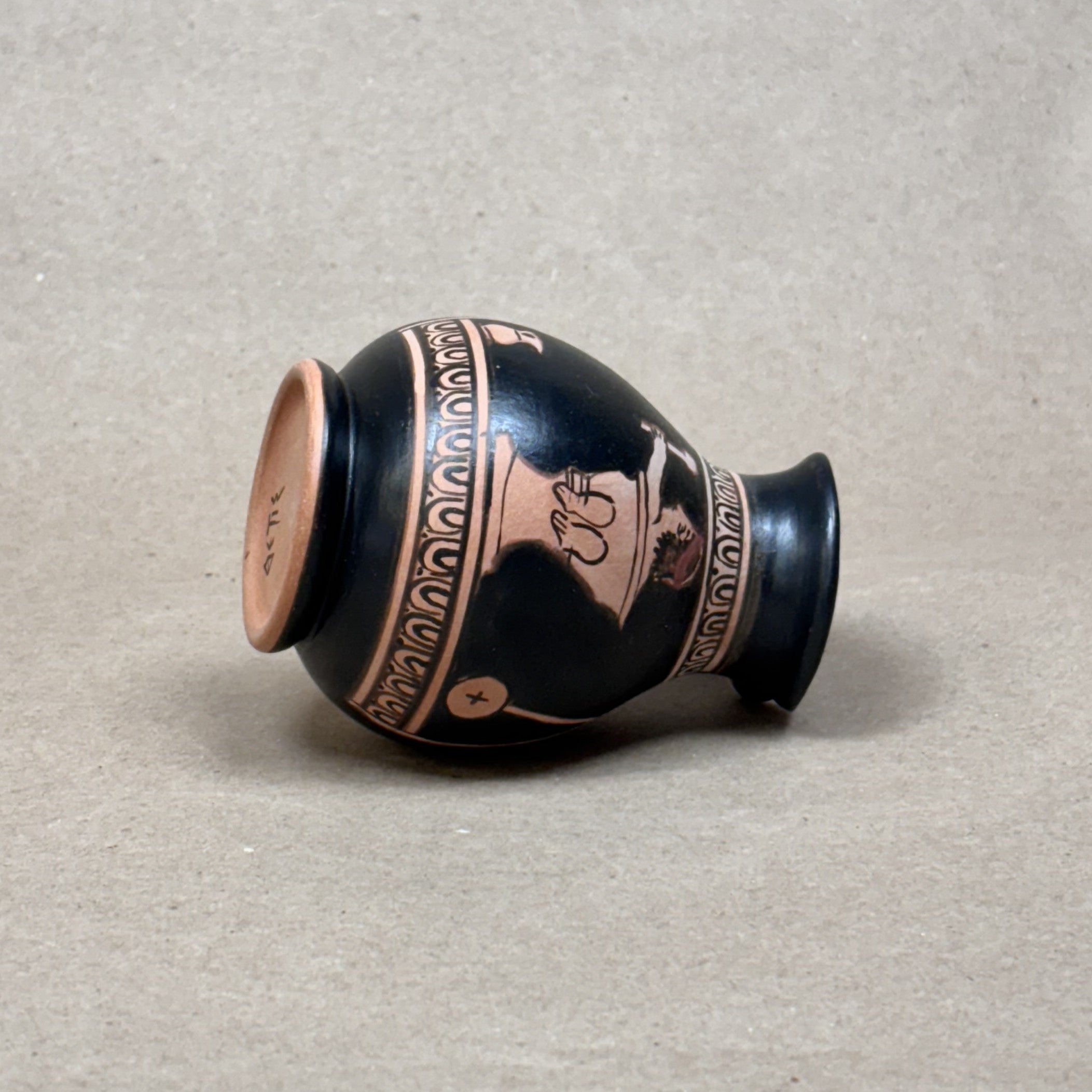 Black ceramic vase with decorative copper patterns on a beige background