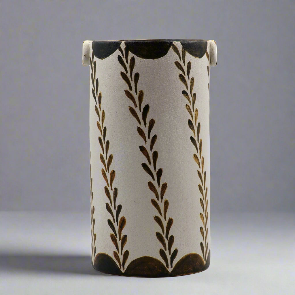 A cylindrical ceramic vase with geometric patterns and brown floral motifs on a white background.