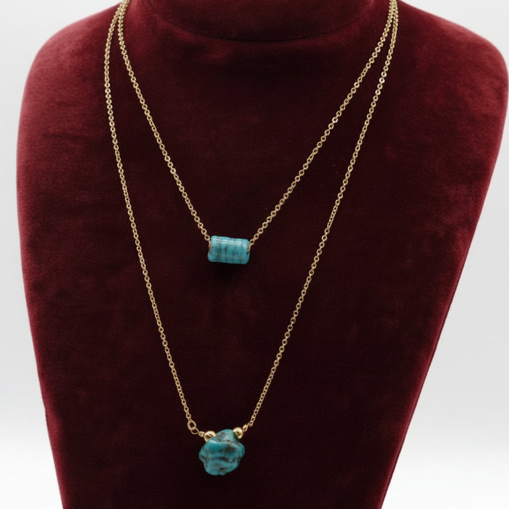 Gold necklaces with turquoise pendants on a red velvet stand.
