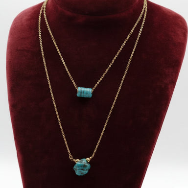 Gold necklaces with turquoise pendants on a red velvet stand.