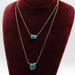 Gold necklaces with turquoise pendants on a red velvet stand.