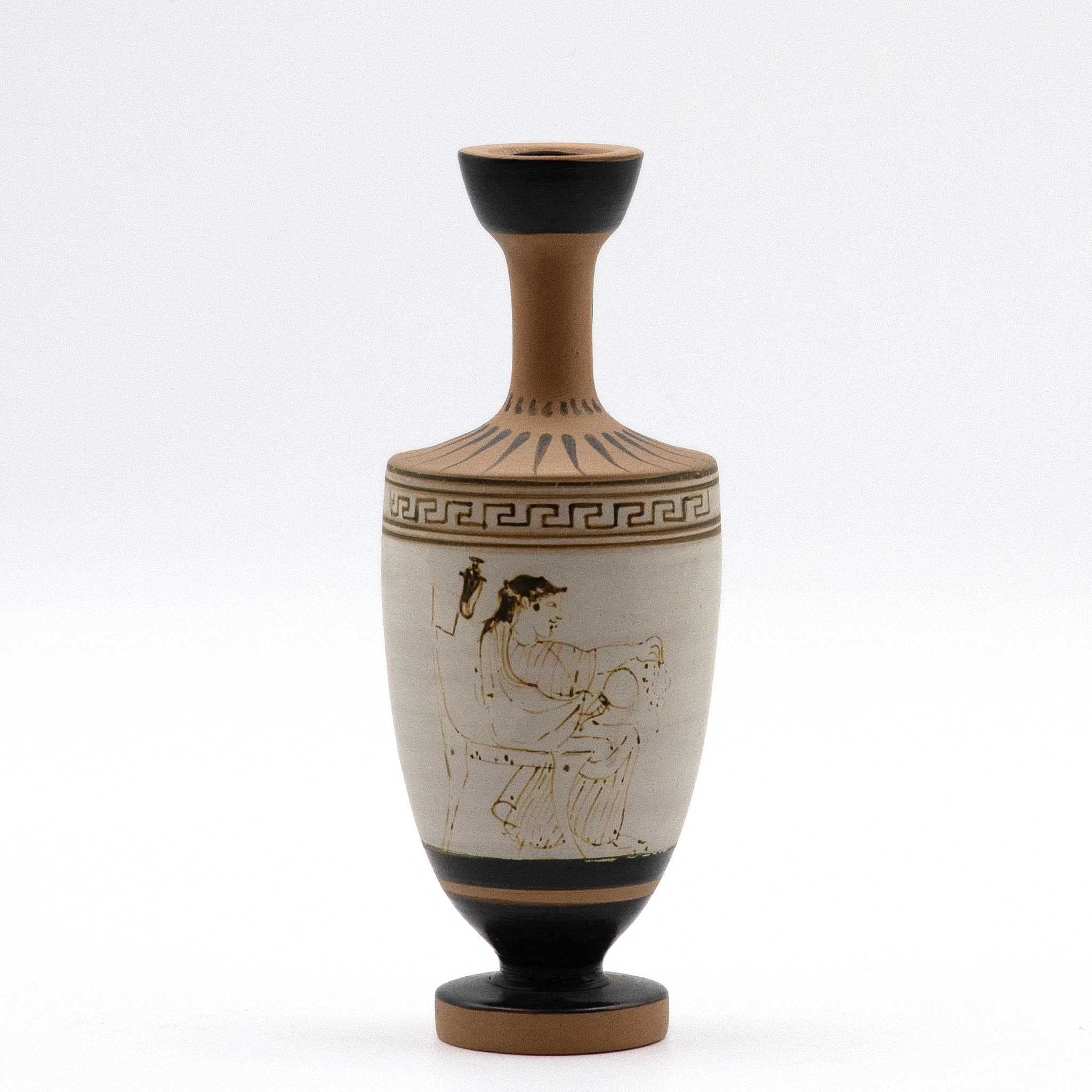 This image features a meticulously crafted white lekythos, a type of oil flask, adorned with a beautifully diluted clay-paint that produces a striking gold-like outline upon firing. The scene depicts a seated woman, dressed in a chiton and himation, engaging with a mirror and a wreath.