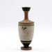 This image features a meticulously crafted white lekythos, a type of oil flask, adorned with a beautifully diluted clay-paint that produces a striking gold-like outline upon firing. The scene depicts a seated woman, dressed in a chiton and himation, engaging with a mirror and a wreath.