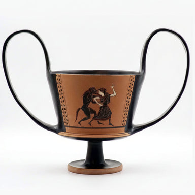 A black figure kantharos vase with a satyr chasing a maenad on one side and Hercules with an Amazon on the other, standing on a round base which is likely to be wooden.