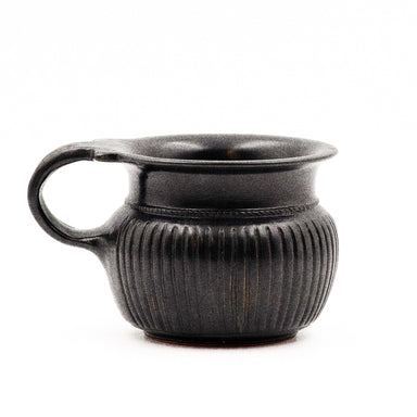 A black glazed ribbed mug with neat reeding and a double handle, reminiscent of ancient Greek pottery.