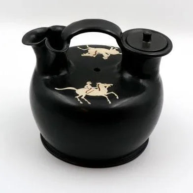 A black glazed ceramic askos with white painted decoration depicting horses. It has two spouts and a lid, resembling an ancient Greek pottery style.