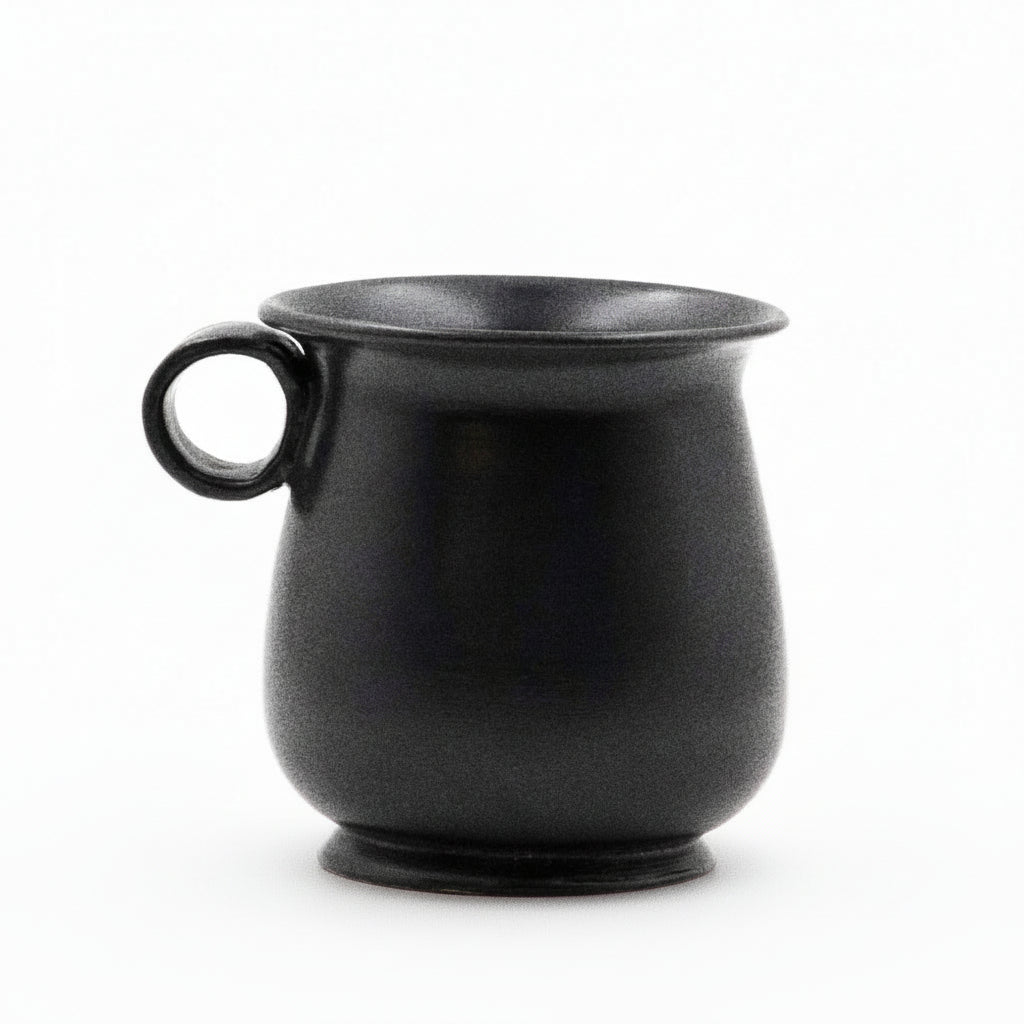 A black glazed ceramic mug with a tulip shape and a handle on the side.