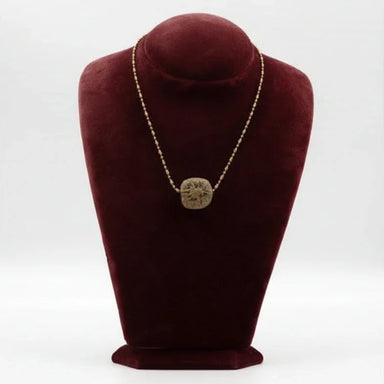 A ceramic pendant necklace displayed on a red velvet mannequin bust. The necklace has a gold-colored chain and a brown, circular pendant.