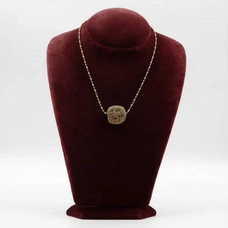 A ceramic pendant necklace displayed on a red velvet mannequin bust. The necklace has a gold-colored chain and a brown, circular pendant.