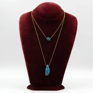 Gold chain necklaces with blue ceramic pendants displayed on a burgundy bust stand