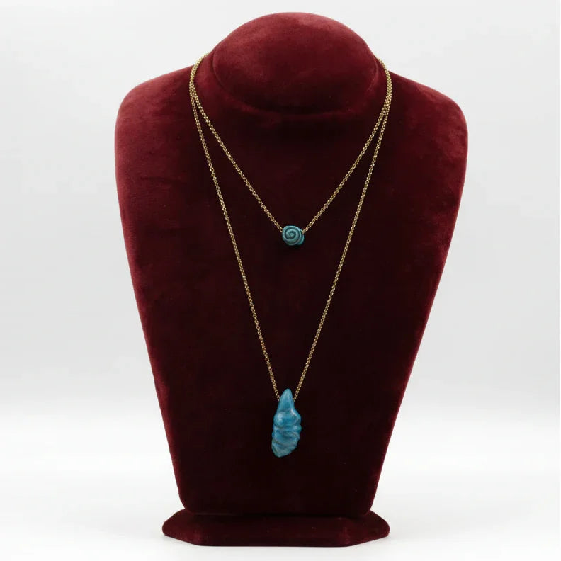 Gold chain necklaces with blue ceramic pendants displayed on a burgundy bust stand
